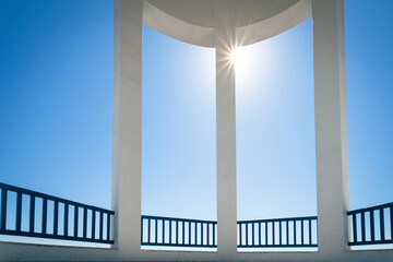 View to blue sky with the sun in shape of a star through columns of a rotunda.