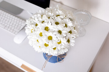 
Beautiful bouquet of chamomile flowers on office desk near computer and glass of water