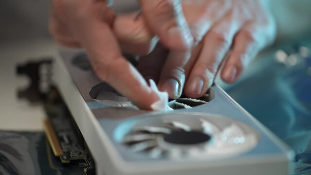Extreme close-up of unrecognizable computer master wiping cooler blades of modern gaming graphics card using small wet rag, during maintenance and service. Shooting in slow motion.