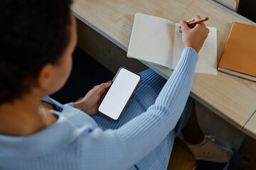 High angle view of student sitting at desk and writing off the mobile phone in notebook during lecture