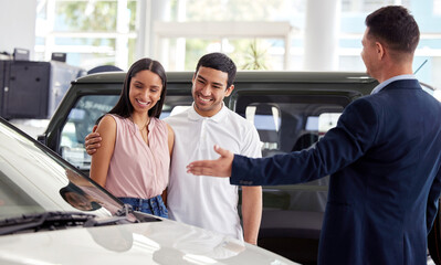 This beauty just came in. a car salesman assisting a young couple on the showroom floor.