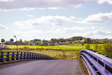 Overpass bridge against blue sky. Asphalt paved road, metal guardrails at midday in warm summer sunny day. Straight pathway goes down over a horizon. Rural street scene. Infrastructure in a village