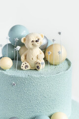 Cake with blue or turquoise velvet cream coating with teddy bear on top. Birthday cake for a little baby with chocolate turquoise and silver spheres on the white background. One year old celebration.