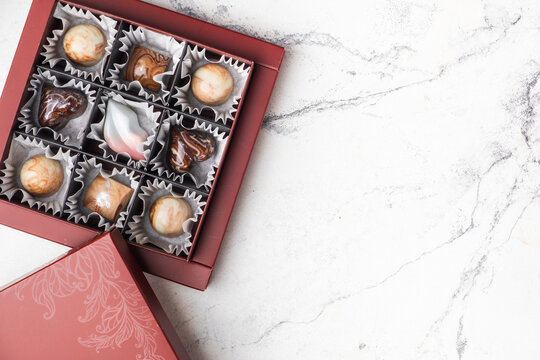 Set of homemade chocolate bonbons in an open gift box. Assortment of hand painted chocolate candy with marble coating. Mockup with a copy space for a free text for chocolatier products.