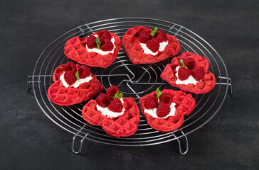 Red heart-shaped waffles with raspberries and micro greenery. On a serving metal stand. Dark gray background. Valentine's Day