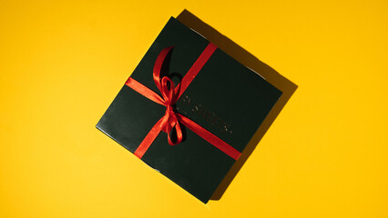 Black gift box tied with a red ribbon on the yellow background. Flat lay. Happy birthday concept. Present in a festive package