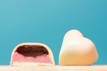Close up of homemade pink heart-shaped chocolate bonbon slice. Assortment of hand painted candies. Candy cut in a half. Mockup with a copy space. Macro shot of  chocolatier products on blue background