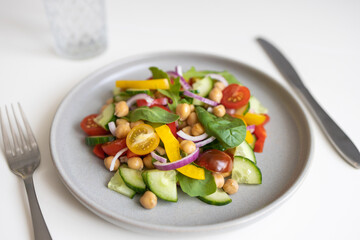 Close-up of a salad of chickpeas and fresh vegetables and lettuce leaves on a white table. Vegetarian food rich in proteins. Ideal for vegans for lunch or dinner.
