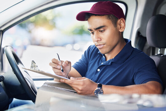 Planning his delivery route for the day. a young delivery man writing on a clipboard while sitting in a van.