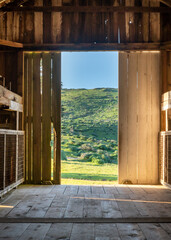 View of green landscape from inside doorway of rustic barn - 596094251