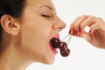Close-up of young woman eating cherries on white background.