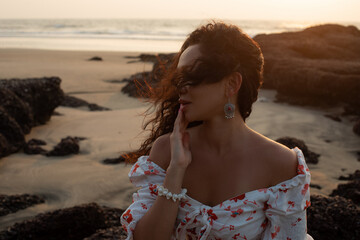 Closeup attractive, seductive woman with blowing messy curls in light summer dress look away against seashore at beach.