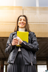 Woman in the street holding documents and a coffee to go. Young woman in jacket holding documents and a coffee in the street