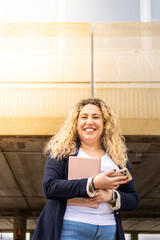 Woman in the street holding tablet and phone looking at camera. Young businesswoman in jacket smiling.