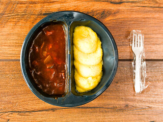 Beef Bourguignon and mash potatoes in a black plastic tray on wooden table and plastic fork. High quality ready meal with premium ingredients for quick lunch warm up in microwave.