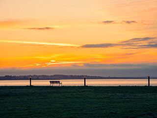 Obraz premium Empty bench by the ocean at sunrise. Warm and cool color.