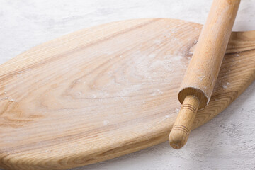 Wooden board sprinkled with flour and a rolling pin on a light gray background