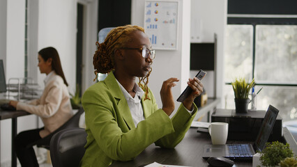 African american employee using mobile phone at work, sitting at desk planning business investment. Young manager checking social media app on smartphone, career development.