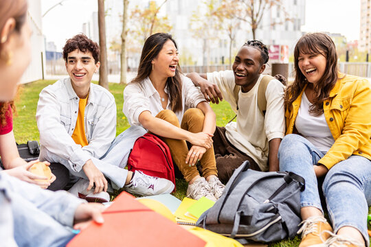 Young group of multiracial students laughing and having fun together sitting on the grass in the university campus. Teenage classmates social gathering relaxing outdoors. - Powered by Adobe