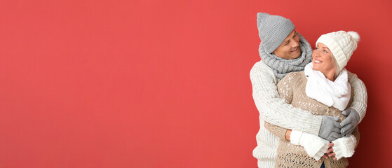 Portrait of happy mature couple in winter clothes on red background with space for text