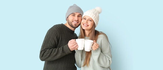 Portrait of happy couple in winter clothes and with cups of hot tea on light background