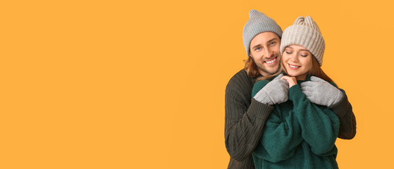 Happy couple in winter clothes on orange background with space for text