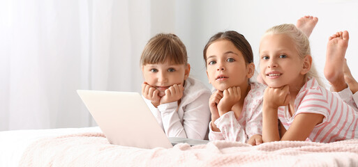 Cute little girls with laptop lying on bed