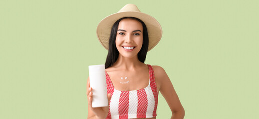 Happy young woman with sunscreen cream on green background