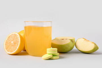 Glass of vitamin C effervescent tablet dissolved in water, apples and lemons on grey background