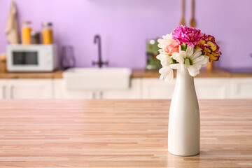Vase with beautiful flowers on wooden table in kitchen