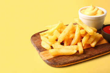 Wooden board with tasty french fries and sauce on color background