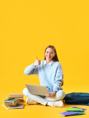 Female student with laptop showing thumb-up on yellow background
