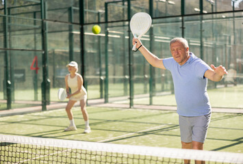 Motivated senior man playing padel with his teammate in court