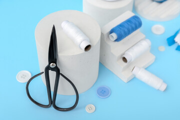 Podiums with scissors, thread spools and buttons on blue background, closeup