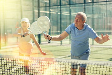Fototapeta premium Active aged man and woman practicing Padel Tennis with other players in the tennis court outdoors