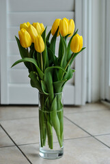 A vase of yellow tulips sits on a tiled floor. A bouquet of yellow tulips.