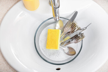 Bowl with cutlery and cleaning sponge in sink, closeup