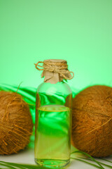 Organic Coconut oil in transparent glass bottles and coconuts with green palm leaves on a green background.Vegetable natural fats. 
