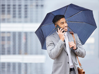 Rain, hail or shine - success is mine. a young businessman holding an umbrella while talking on a cellphone on a rainy day in the city.