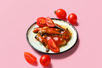 Plate with canned fish in sauce and tomatoes on pink background