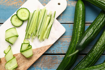 Fresh cucumbers and cut pieces on blue wooden background, closeup
