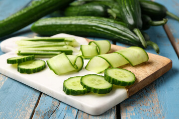 Board with fresh cut cucumber on blue wooden background, closeup