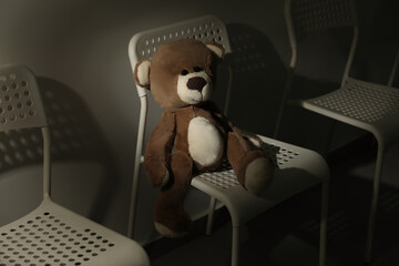 Cute lonely teddy bear on chair in dark room. Space for text
