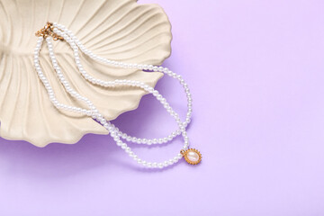 Decorative plate in shape of leaf with pearl necklaces on lilac background, closeup