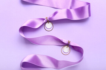 Ribbon with golden earrings on lilac background