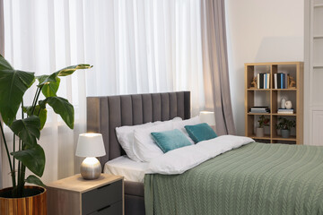 Comfortable bed with bedding, houseplants and books in room