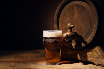 Wooden barrel and glass of cold beer on table against dark background
