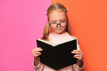 Cute little girl in glasses with book on colorful background