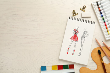 Sketches of different clothes in pad on white wooden table, space for text. Fashion designer's desk...