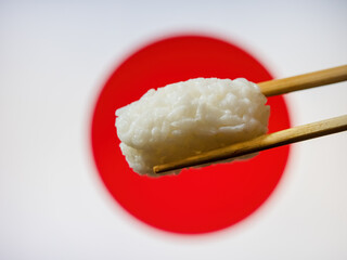 Taste of Japan: Savoring Sushi Rice, a Staple of Japanese Cuisine, Between Chopsticks, Set Against the Iconic Japanese Flag